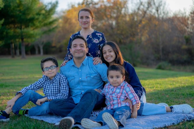 A smiling family sitting outside on a picnic blanket.